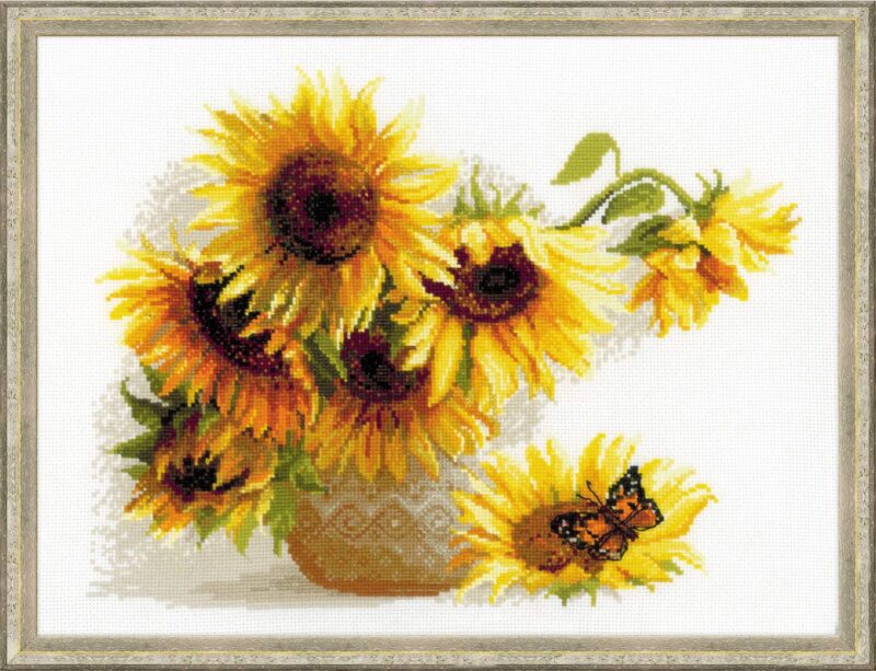 A cross-stitch artwork of bright sunflowers in a vase, with a butterfly resting on a fallen bloom, stitched on white fabric.