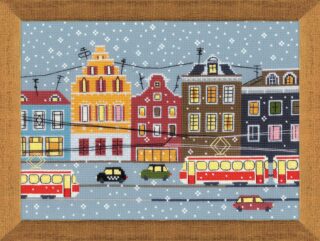 A cross-stitch artwork of colorful city buildings with red and yellow trams moving through snowy streets, stitched on blue fabric.