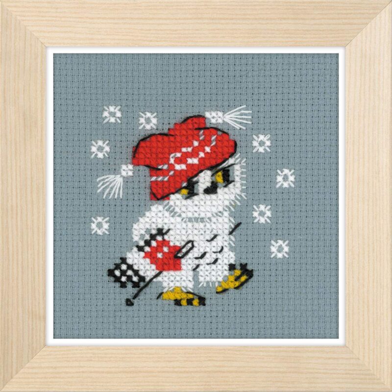 Cross-stitched owl skiing in a red winter hat and mittens, surrounded by falling snowflakes on gray fabric.
