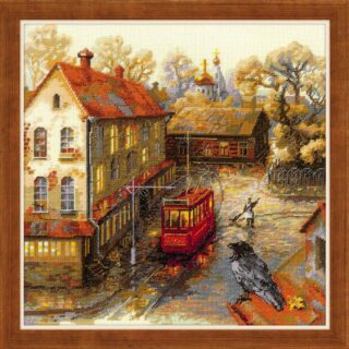 Cross-stitched autumn cityscape with golden trees, a red tram, historic buildings, and a crow perched on a rooftop in warm fall tones.