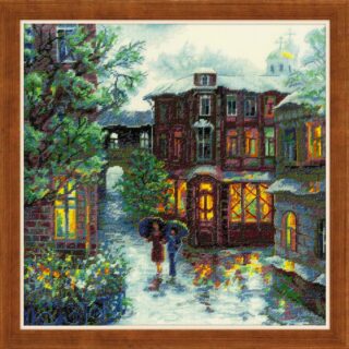 Cross-stitched romantic city scene with glowing windows, two people under umbrellas, blooming flowers, and reflections on wet cobblestone streets.