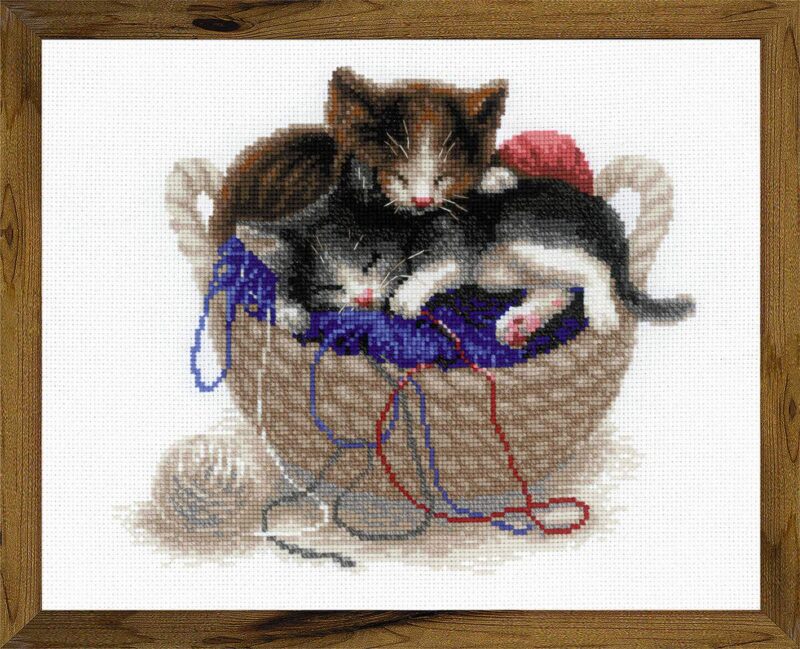 Two kittens nap together in a woven basket surrounded by colorful yarn in this adorable cross-stitch design.