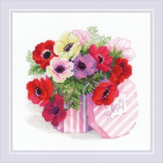 A striped pink gift box overflowing with colorful anemones in red, white, purple, and pink, with the word "Merci" stitched on the lid.
