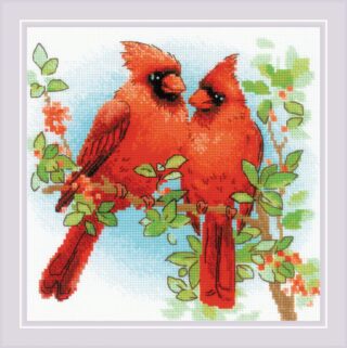 Two bright red cardinals perched on a leafy branch with a soft blue sky in the background.