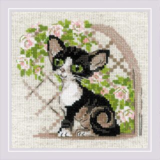 A playful Cornish Rex kitten with large ears and bright green eyes sits near pink climbing roses on a trellis in this cross-stitch design.