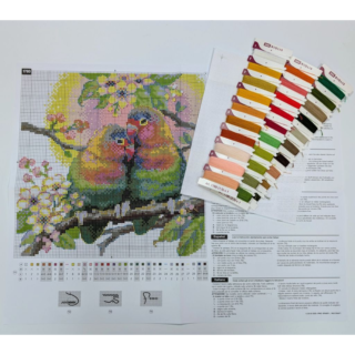 A cross-stitched pair of colorful lovebirds cuddling on a flowering tree branch with green leaves and white blossoms.