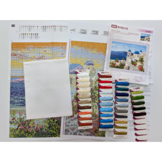 Cross stitch design of a sunny coastal scene in Santorini with white buildings, blue domes, and flowering plants by the sea.