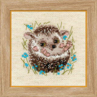 A smiling baby hedgehog sits in tall grass surrounded by bright blue flowers in a charming cross-stitch design.