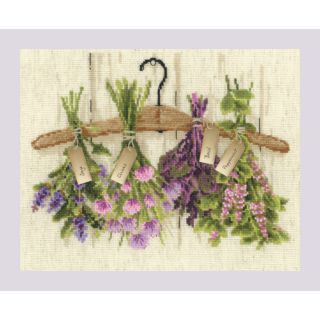 A cross-stitched hanger with bundles of herbs labeled sage, chives, basil, and peppermint, hanging in front of a rustic background.