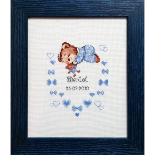 Cross-stitch design featuring a sleeping baby bear in blue pajamas surrounded by blue hearts, bows, and birth details.