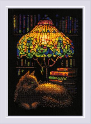 Cross-stitch of a cat resting beside a glowing stained-glass lamp, with books and shelves in the background, stitched on black fabric.