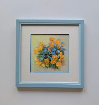 Framed embroidery of a vibrant bouquet with golden-yellow flowers and light blue blossoms on a soft background.