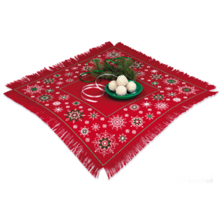 A red table topper with white and green embroidered snowflake patterns, fringed edges, and a festive holiday arrangement in the center.