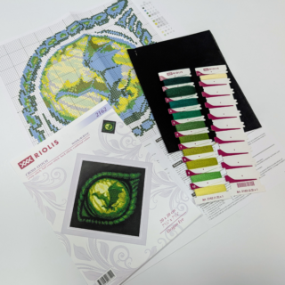 Close-up of a green dragon’s eye with a dragon silhouette in its glowing pupil, stitched on black fabric.