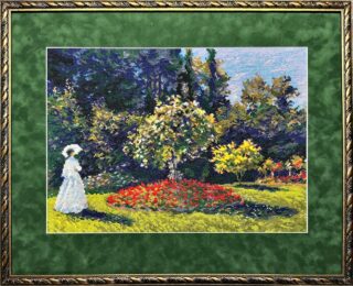 Framed embroidery of a woman in a white dress standing near a flowering tree in a colorful garden with bright flowerbeds and green lawns.