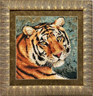 Framed embroidery of a tiger’s face with striking golden eyes, detailed stripes, and a natural background.