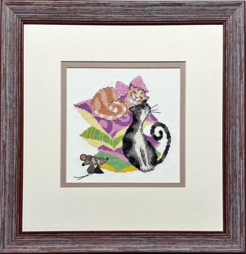 Framed embroidery of two cats resting on colorful pillows with a small mouse nearby, stitched in bright and playful colors.