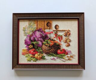 Framed embroidery of a rustic still life with a basket of vegetables, garlic, and peppers in a warm kitchen setting.