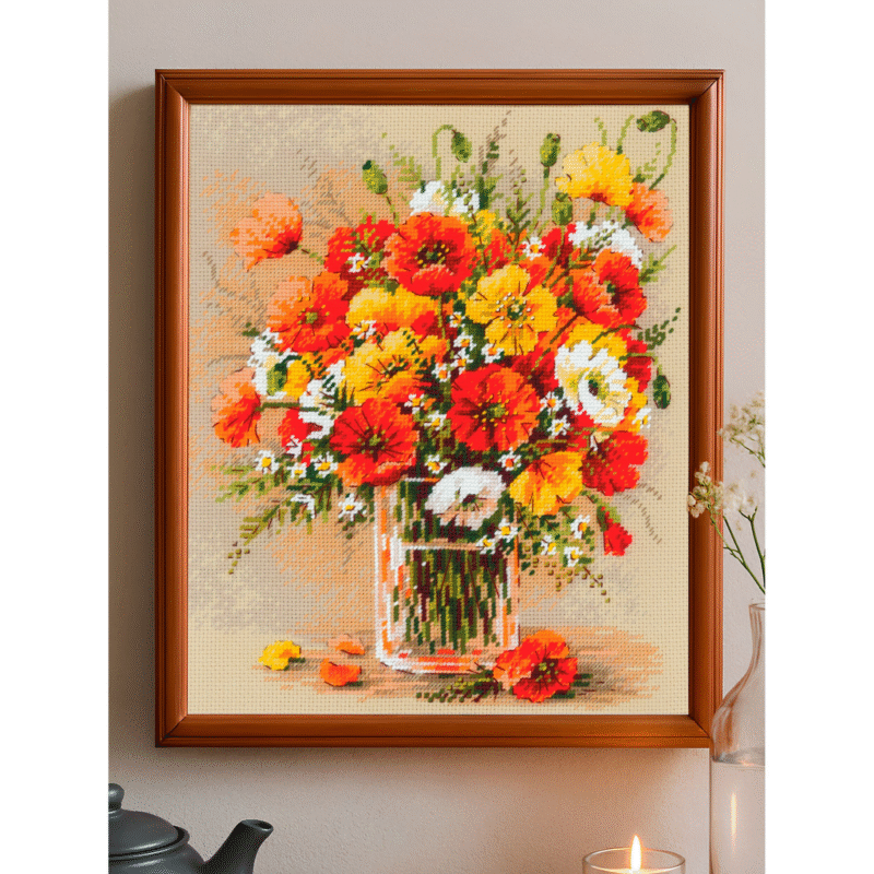 A vibrant cross-stitched bouquet of red, yellow, and white field poppies arranged in a glass vase, with scattered petals around the base.