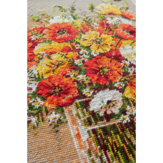 A vibrant cross-stitched bouquet of red, yellow, and white field poppies arranged in a glass vase, with scattered petals around the base.