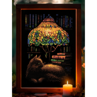 Cross-stitch of a cat resting beside a glowing stained-glass lamp, with books and shelves in the background, stitched on black fabric.