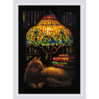 Cross-stitch of a cat resting beside a glowing stained-glass lamp, with books and shelves in the background, stitched on black fabric.