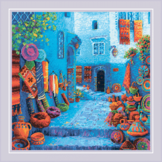 Cross-stitch design of a vibrant Moroccan street filled with colorful pottery, textiles, rugs, and architectural details in vivid blues and warm earth tones.