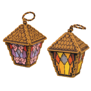 Two vintage-style cross-stitched lantern ornaments in warm purple, pink, yellow, and orange, stitched on plastic canvas with hanging loops.