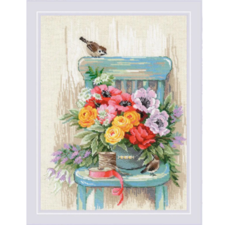 Cross-stitch of a bouquet of colorful garden flowers arranged on a teal chair with two small birds, a spool of thread, and ribbon beside it.