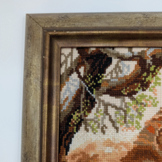 Framed cross-stitch artwork showing a majestic lion resting under trees in a warm savanna landscape.