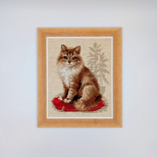 Framed cross-stitch artwork of a fluffy brown and cream cat sitting on a red cushion against a neutral background.