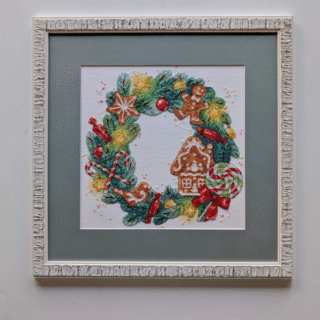 Framed cross-stitch artwork of a Christmas wreath decorated with gingerbread cookies, candy canes, bows, and festive holiday details.