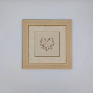 Framed cross-stitch artwork of a delicate floral heart with pastel flowers and a central date, stitched in soft neutral tones.