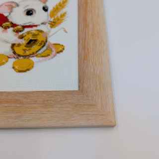 Framed cross-stitch artwork of a white mouse holding a coin and a wheat stalk, sitting among golden coins on a light background.