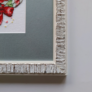 Framed cross-stitch artwork of a Christmas wreath decorated with gingerbread cookies, candy canes, bows, and festive holiday details.