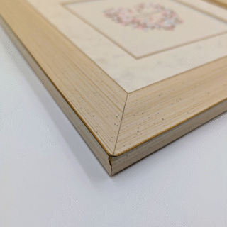 Framed cross-stitch artwork of a delicate floral heart with pastel flowers and a central date, stitched in soft neutral tones.