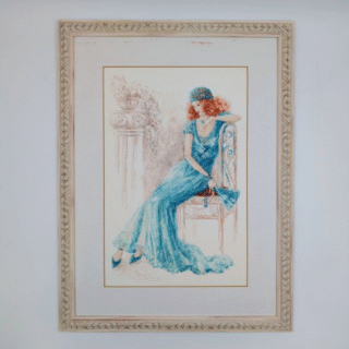Framed cross-stitch artwork depicting an elegant woman in a flowing turquoise evening gown seated on a chair in a vintage, classic interior.