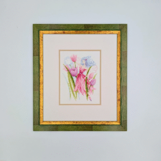 Framed cross-stitch artwork of a spring fairy surrounded by pink flowers and green stems in soft pastel tones.