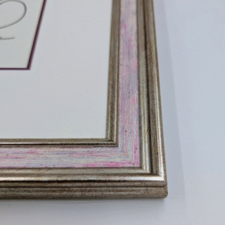 Framed cross-stitch artwork featuring a stylized bird with flowing decorative feathers in vibrant blue, pink, and orange patterns.