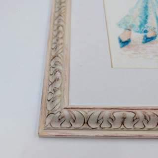 Framed cross-stitch artwork depicting an elegant woman in a flowing turquoise evening gown seated on a chair in a vintage, classic interior.