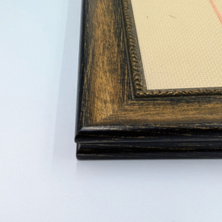 Framed cross-stitch artwork showing a small bird perched on a flowering branch with white blossoms and soft autumn-toned leaves.