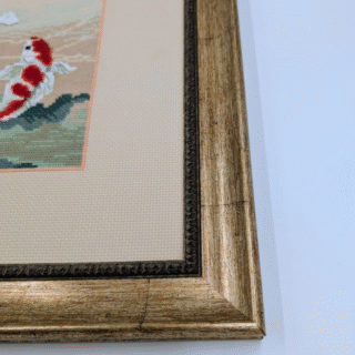 Framed cross-stitch artwork showing red and white koi fish swimming among flowing waves beneath flowering branches.