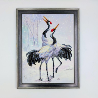 Framed stitched artwork showing two elegant cranes dancing in a snowy winter landscape with soft pastel tones.