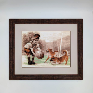 Stitched and framed embroidery artwork showing a young boy holding a football while two playful dogs run and splash nearby on a grassy field.