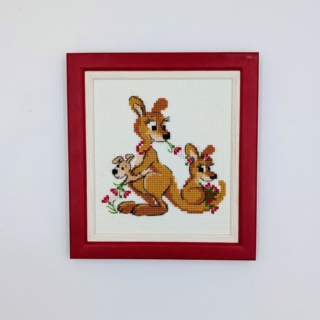 Stitched and framed embroidery artwork depicting a kangaroo family with joeys and flowers on a light background.
