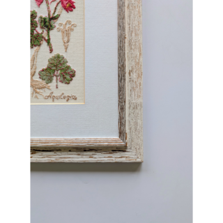 Stitched and framed embroidery artwork featuring elegant pink flowers with detailed leaves on a light fabric background.