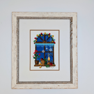 Framed stitched artwork showing a cozy winter window scene with potted plants, yarn, candles, and soft lights against a deep blue evening sky.