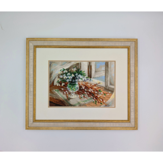 Stitched and framed embroidery artwork showing a vase of white snowdrops on a table beside a sunlit window.