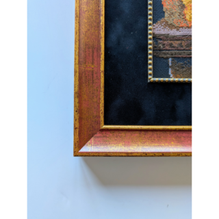 Stitched and framed embroidery artwork depicting a still life with cheese, grapes, fruit, and a wine goblet on a dark background.