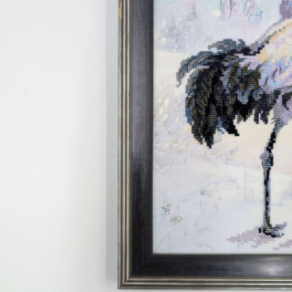 Framed stitched artwork showing two elegant cranes dancing in a snowy winter landscape with soft pastel tones.
